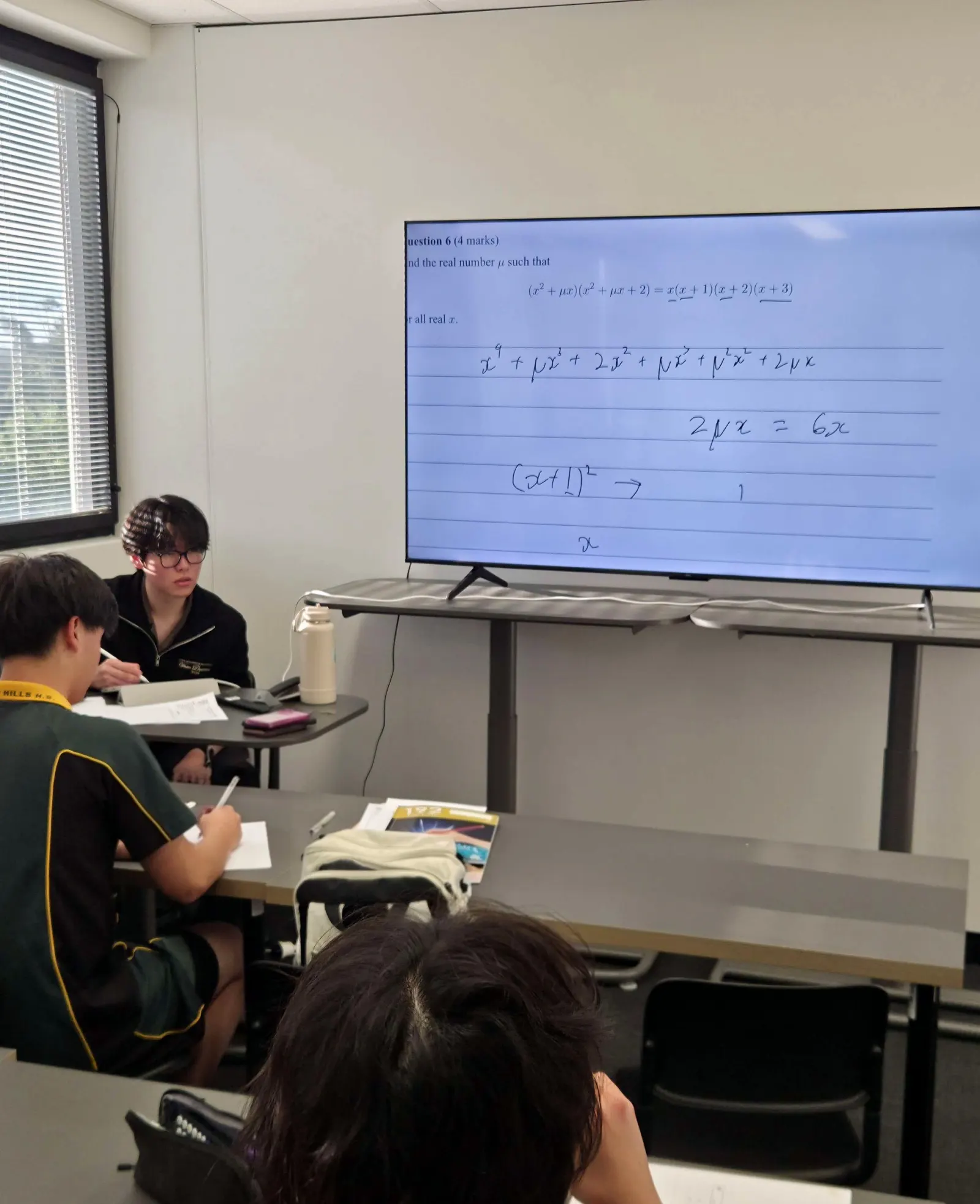 Students working through a question shown on the classroom screen