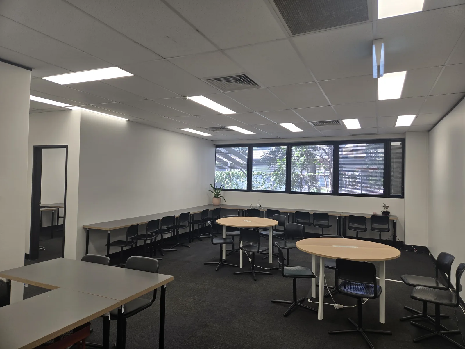 Inside BEAM’s Epping centre, with round tables, classroom desks and windows along the far wall